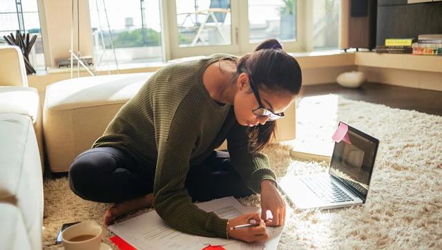 Woman sitting on floor with laptop and study notes