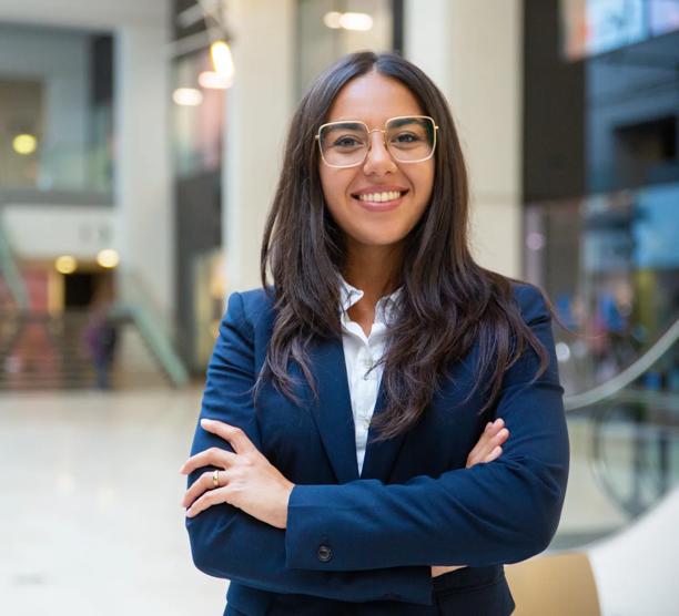 Happy successful businesswoman posing in office hall. Young Latin woman wearing formal suit and glasses, standing for camera with arms folded, smiling. Business portrait concept