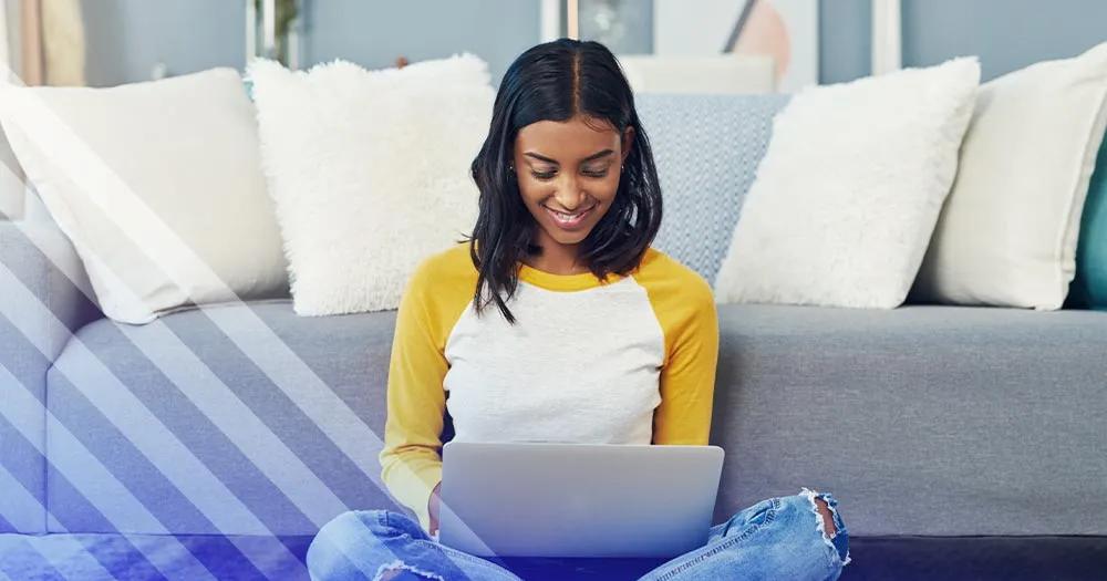 Student sitting on the floor with a laptop, studying online from home.