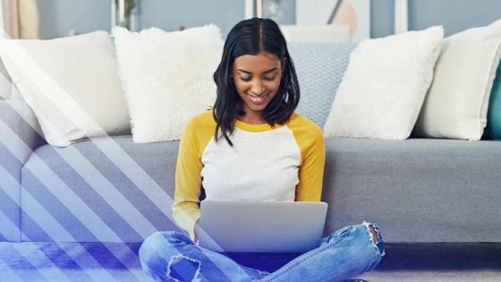 Student sitting on the floor with a laptop, studying online from home.