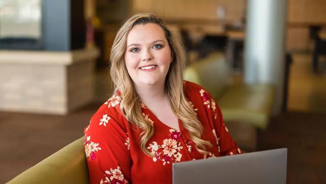 A smiling female ODU student seated on a padded bench with an ODU laptop computer open on her lap.