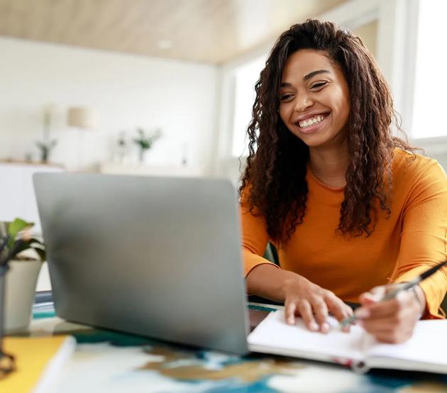 Woman in gold sweater sits at a desk and smiles at her computer while writing