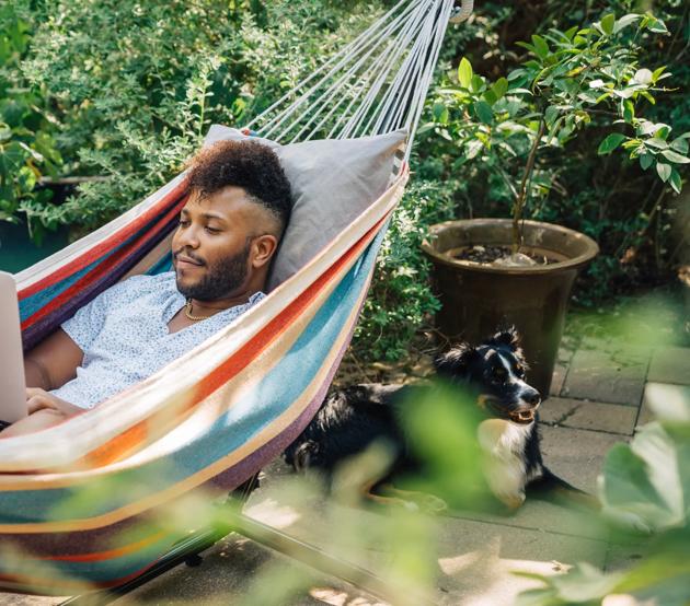 Man working from home on laptop computer while relaxing in hammock in the back yard