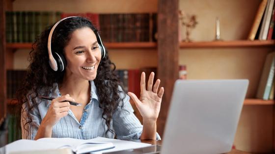 Faculty waving at computer seated at a desk with books