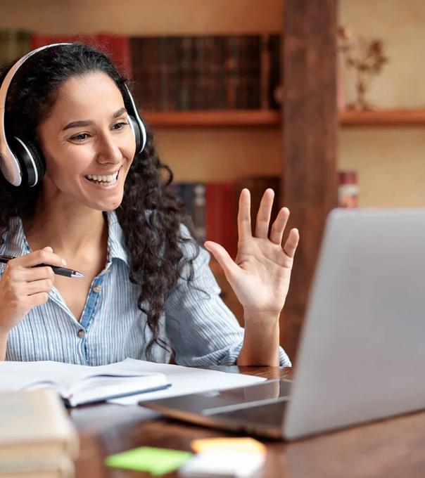 Faculty waving at computer seated at a desk with books
