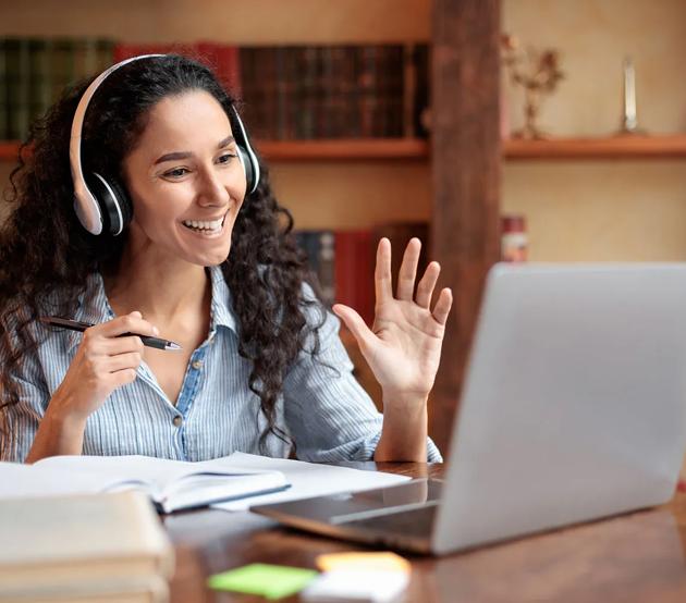 Faculty waving at computer seated at a desk with books