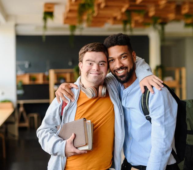 A young man with Down's syndrome and his friend pose together for a happy photo at school.