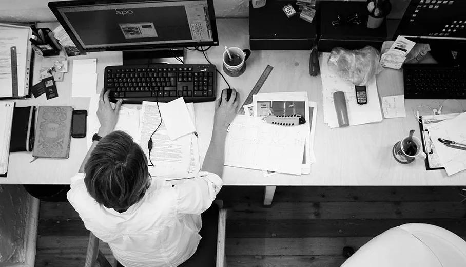 Overhead view of a student working at a desk with a computer, keyboard, papers, and coffee.