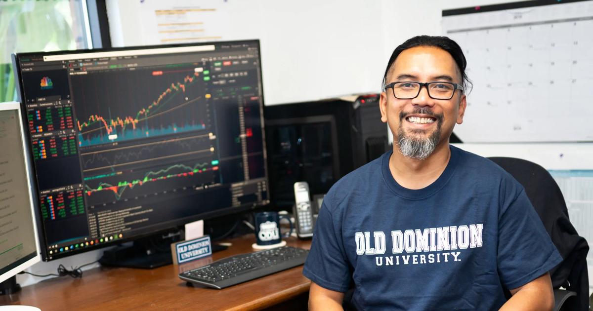 ODU alum and Army veteran Savann Thorne at his desk with financial charts on screen.