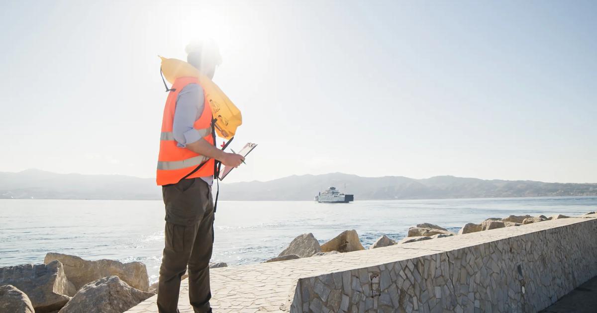 An engineer holding a clipboard stands on a seawall and looks out toward the water.