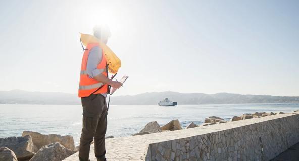 An engineer holding a clipboard stands on a seawall and looks out toward the water.