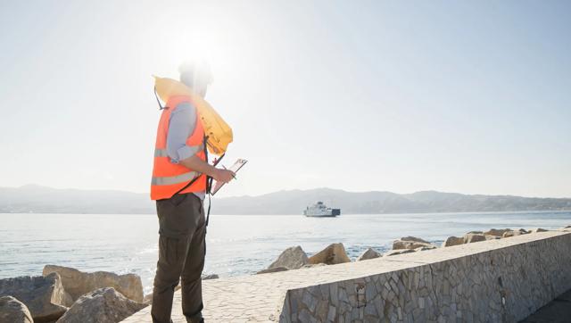An engineer holding a clipboard stands on a seawall and looks out toward the water.