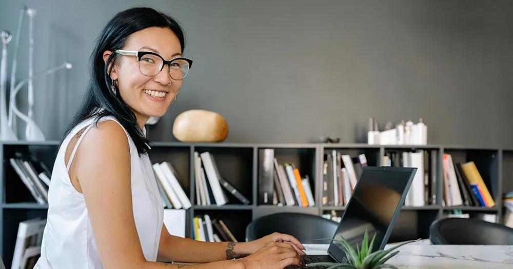 A smiling business women is seated at an office table with a laptop