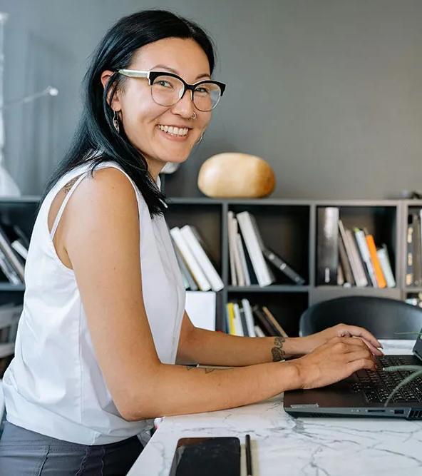 A smiling business women is seated at an office table with a laptop