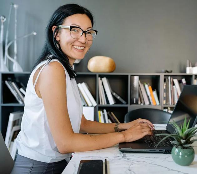 A smiling business women is seated at an office table with a laptop