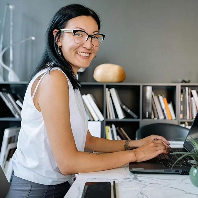 A smiling business women is seated at an office table with a laptop