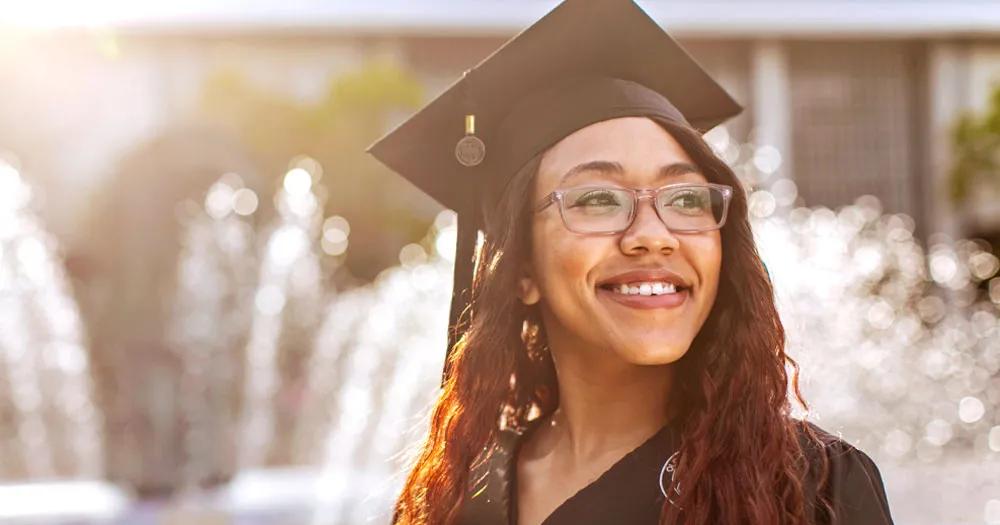 Graduate wearing cap and gown smiling outdoors after earning an undergraduate degree.