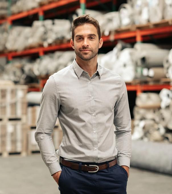 A supply chain manager stands in front of warehouse shelves stacked with building supplies.