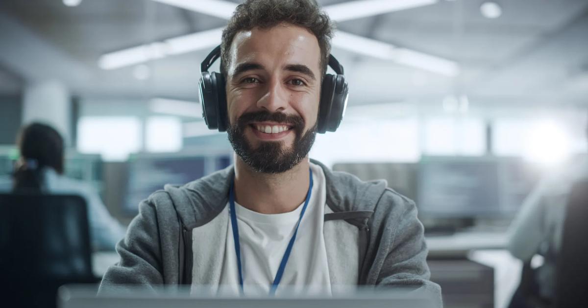 Smiling student wearing headphones, attending an online class on a laptop.