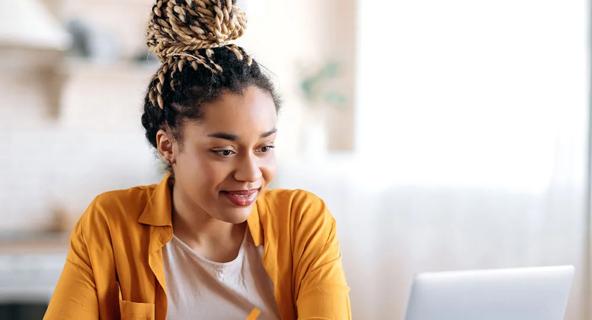 Student taking notes while attending an online class for an interdisciplinary studies degree on a laptop. 
