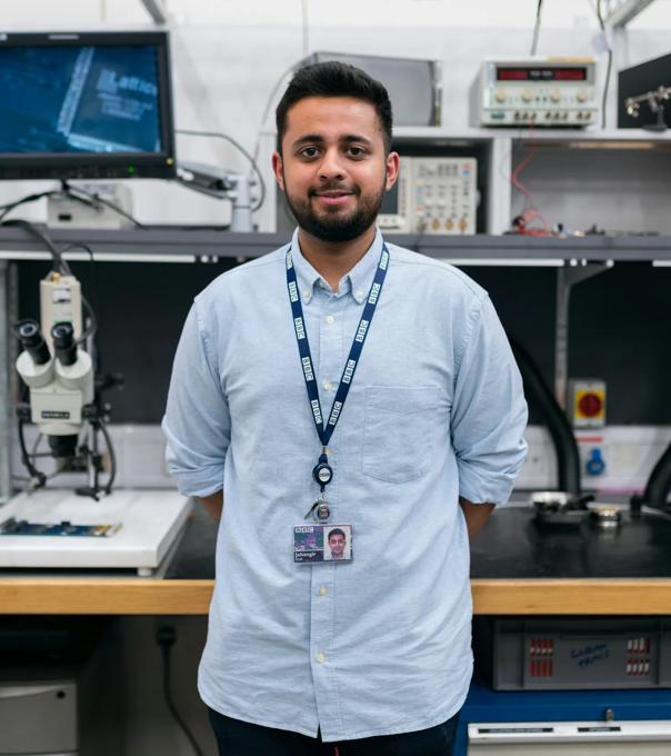 Man standing and smiling in an engineering lab.