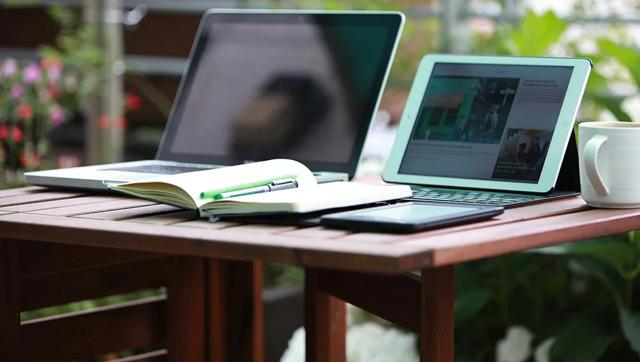 Two open laptops on a wooden desk with a paper notebook nearby