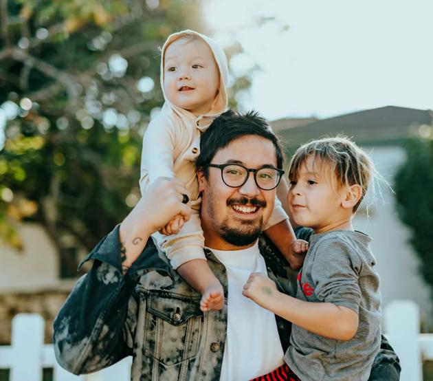 A young dad has fun with his two toddlers outside