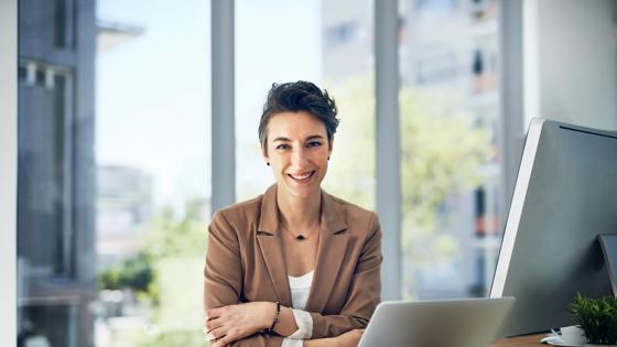 Woman in a blazer smiling at her desk.