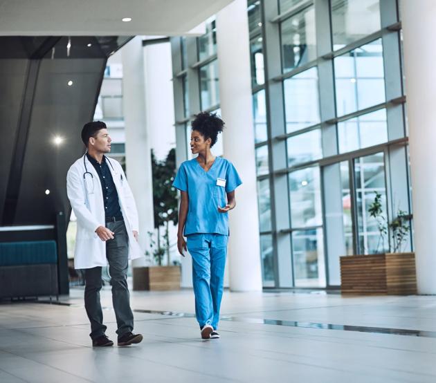Two medical professionals in clinic uniforms talk together as they walk through a health facility.