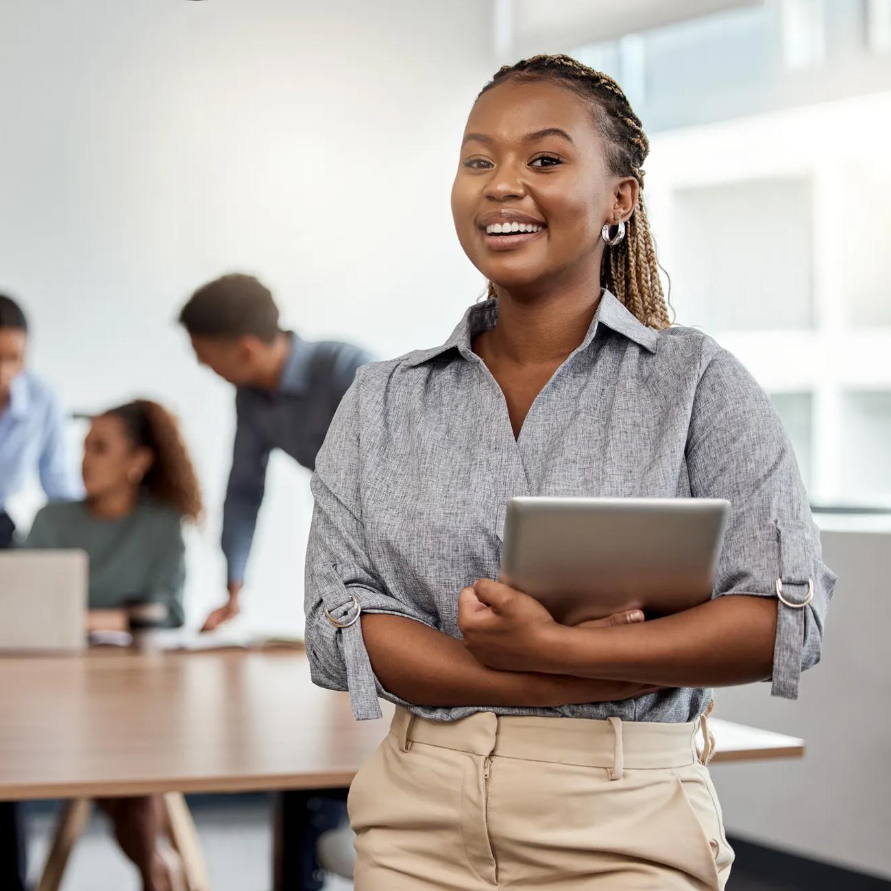 Woman with tablet in a boardroom with colleagues meeting behind her