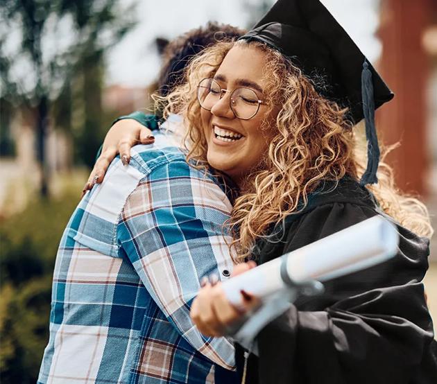 Happy college graduate hugs a family member outside on a sunny day.