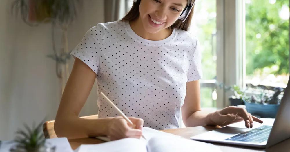 Student wearing headphones taking notes during an online class.