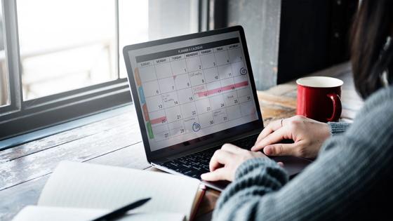 Person sitting at computer organizing a calendar with a journal nearby