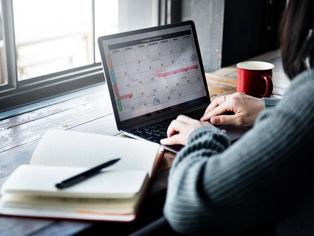 Person sitting at computer organizing a calendar with a journal nearby