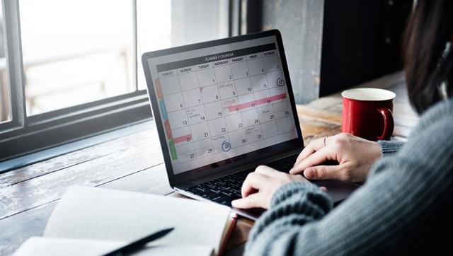 Person sitting at computer organizing a calendar with a journal nearby