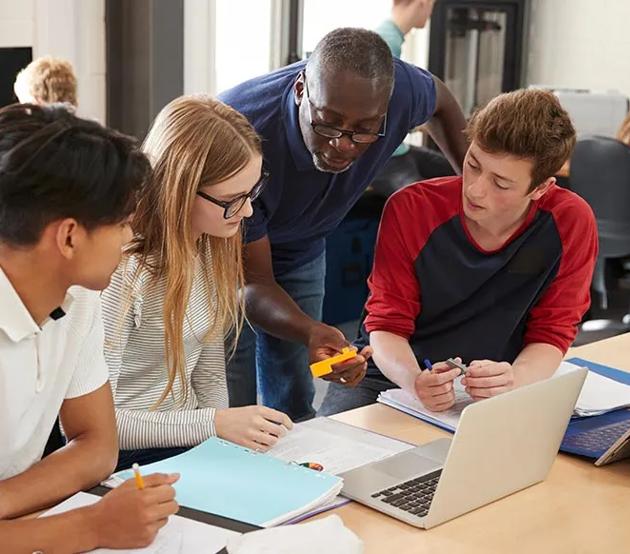 A high school technology teacher advises a group of students in the classroom