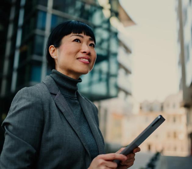 Businesswoman holding tablet and looking up at buildings in the city