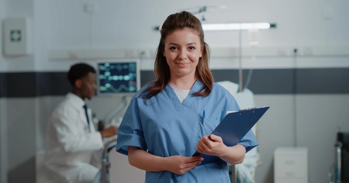 A certified medical assistant poses proudly in a standardized patient practice room.