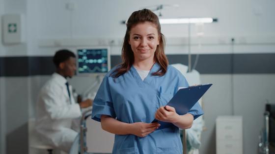 A certified medical assistant poses proudly in a standardized patient practice room.