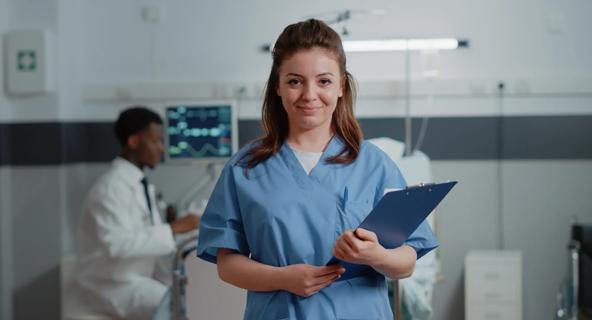 A certified medical assistant poses proudly in a standardized patient practice room.