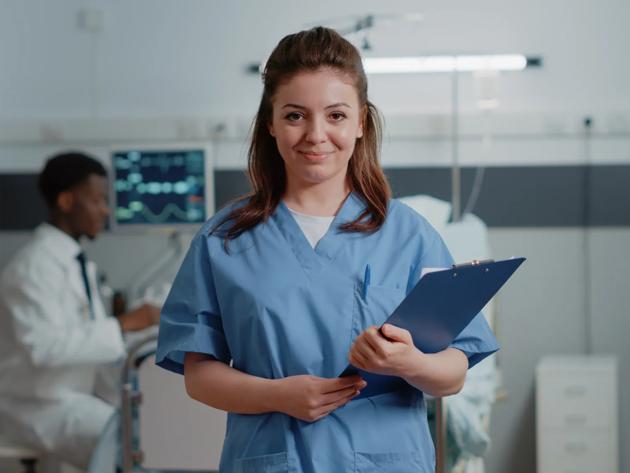 A certified medical assistant poses proudly in a standardized patient practice room.