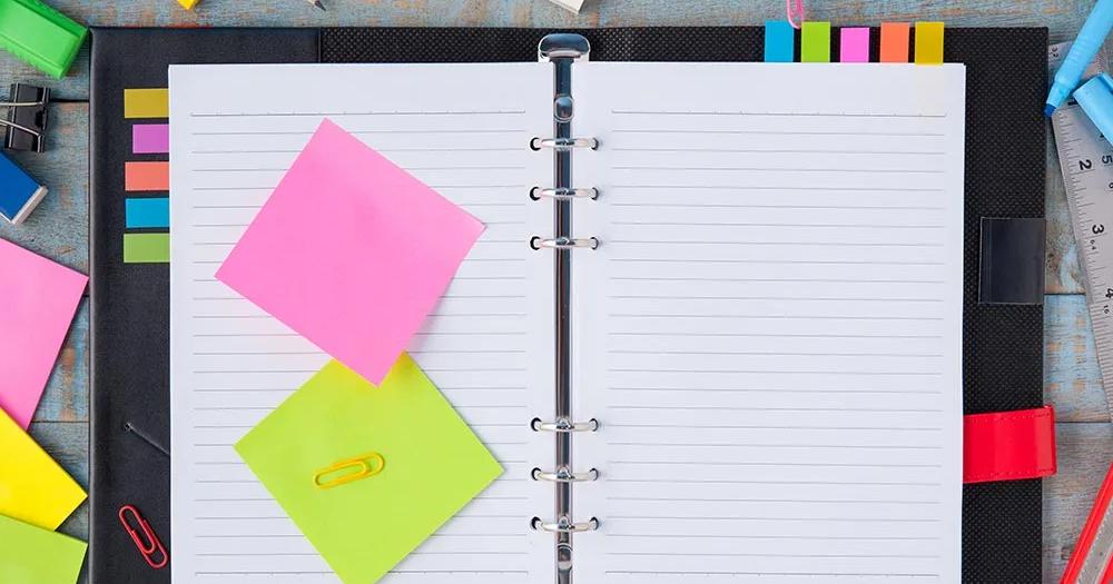Open binder with lined paper, sticky notes, and colorful pens arranged neatly on a desk.