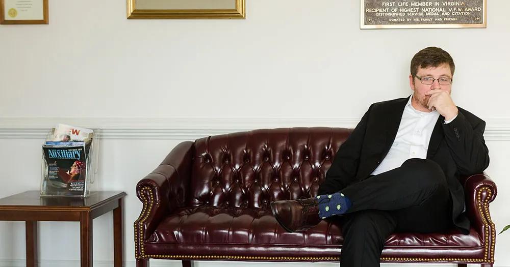 ODU alumnus Ken Wiseman sitting on a leather couch in an office, dressed in a suit.