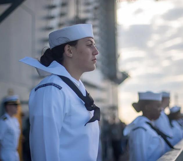 Enlisted Navy personnel stand at attention on the deck of a ship at sea.