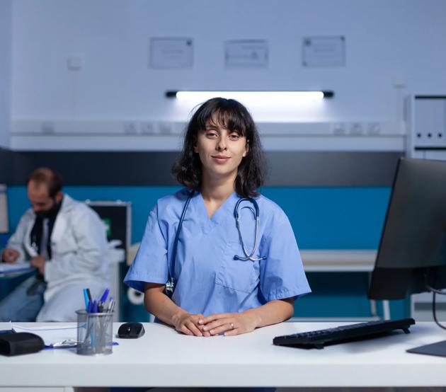 Physician Assistant standing at the nursing station at the hospital, near a doctor on call.