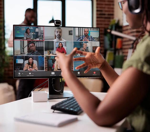 A woman seated at a computer gestures with her hands as she talks to classmates online